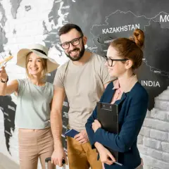 Para z paszportem i modelką samolotu przed mapą świata, obok pracownicy biura podróży.