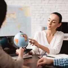 Kobieta w biurze podróży pokazuje klientom globus i mapę.